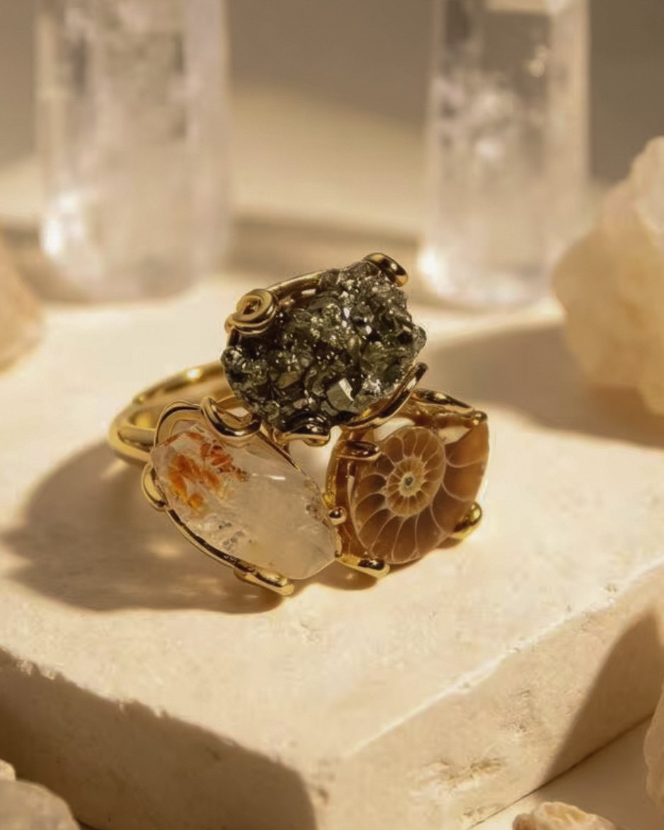 Aurelia — raw crystal ring with a russet-flecked clear crystal, a metallic raw stone and a spiral-patterned stone in a gold-toned setting