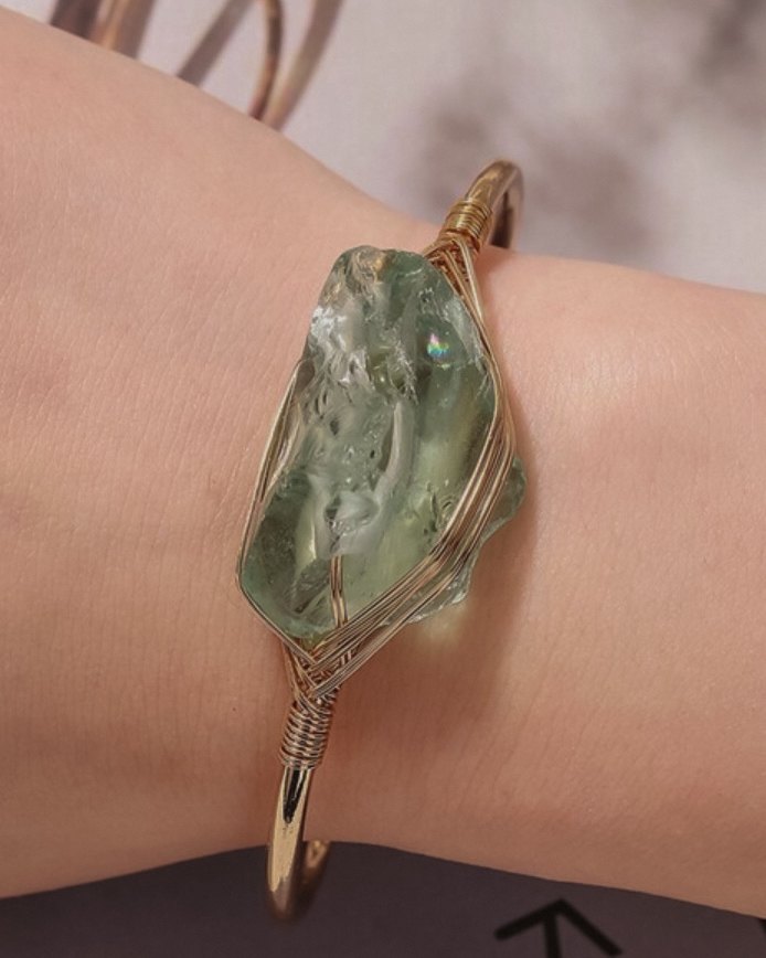 Celeste — raw crystal bracelet: a pale sea-green natural stone wrapped in fine gold-toned wire on an open cuff, worn on the wrist