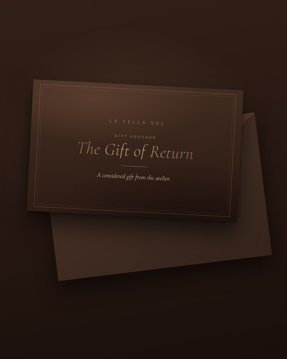 The Gift of Return — La Vella Sol gift voucher card in deep walnut and brushed bronze, resting on an envelope