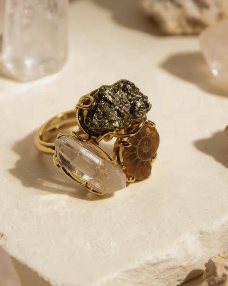 Terra — raw crystal ring with a metallic raw stone, a clear crystal point and a spiral-patterned stone in a gold-toned setting